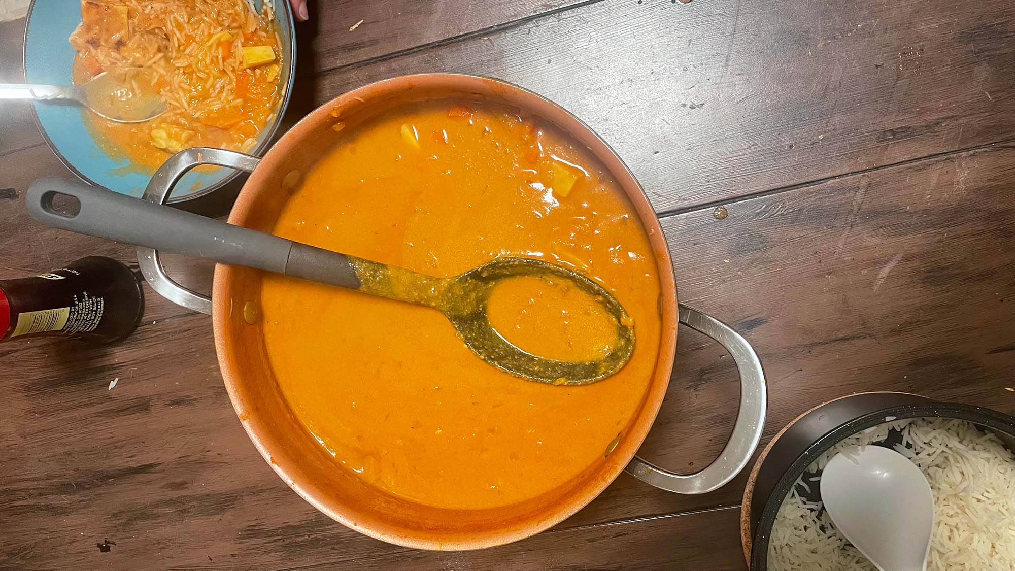 A pot of bright orange peanut stew in a pot, with rice on the side.