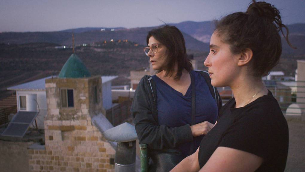 two women with dark hair, one older and one her adult daughter, stand on a rooftop overlooking a Middle Eastern city