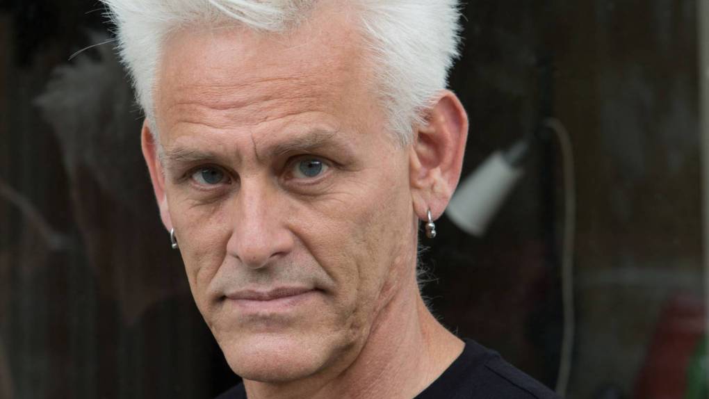 Jess Curtis, a white man with short white hair and a black T-shirt, looks into the camera.