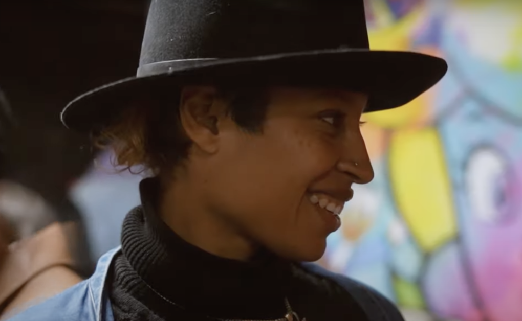 A woman of color wearing a hat, viewed in close up side profile, smiling.