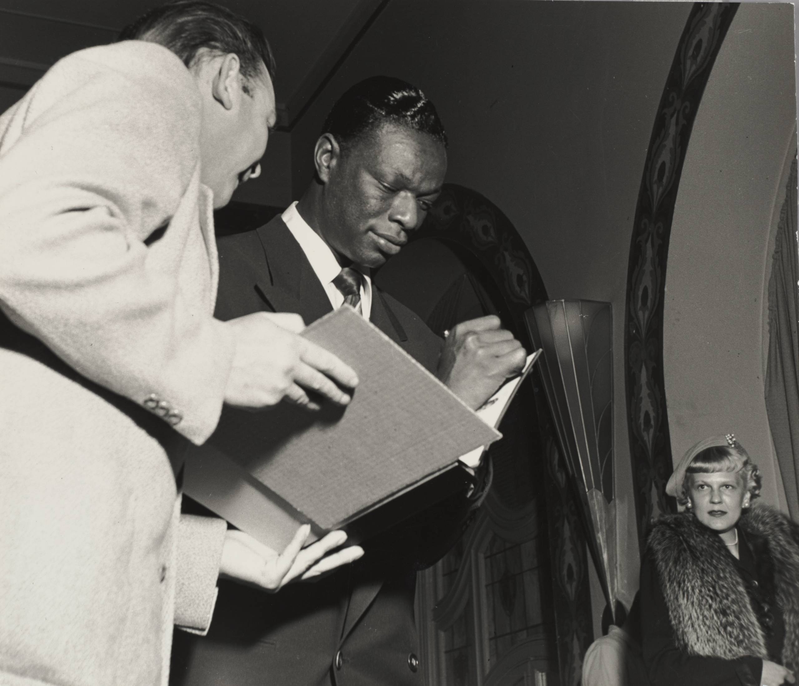 Black-and-white photo of a man signing a book held by another person