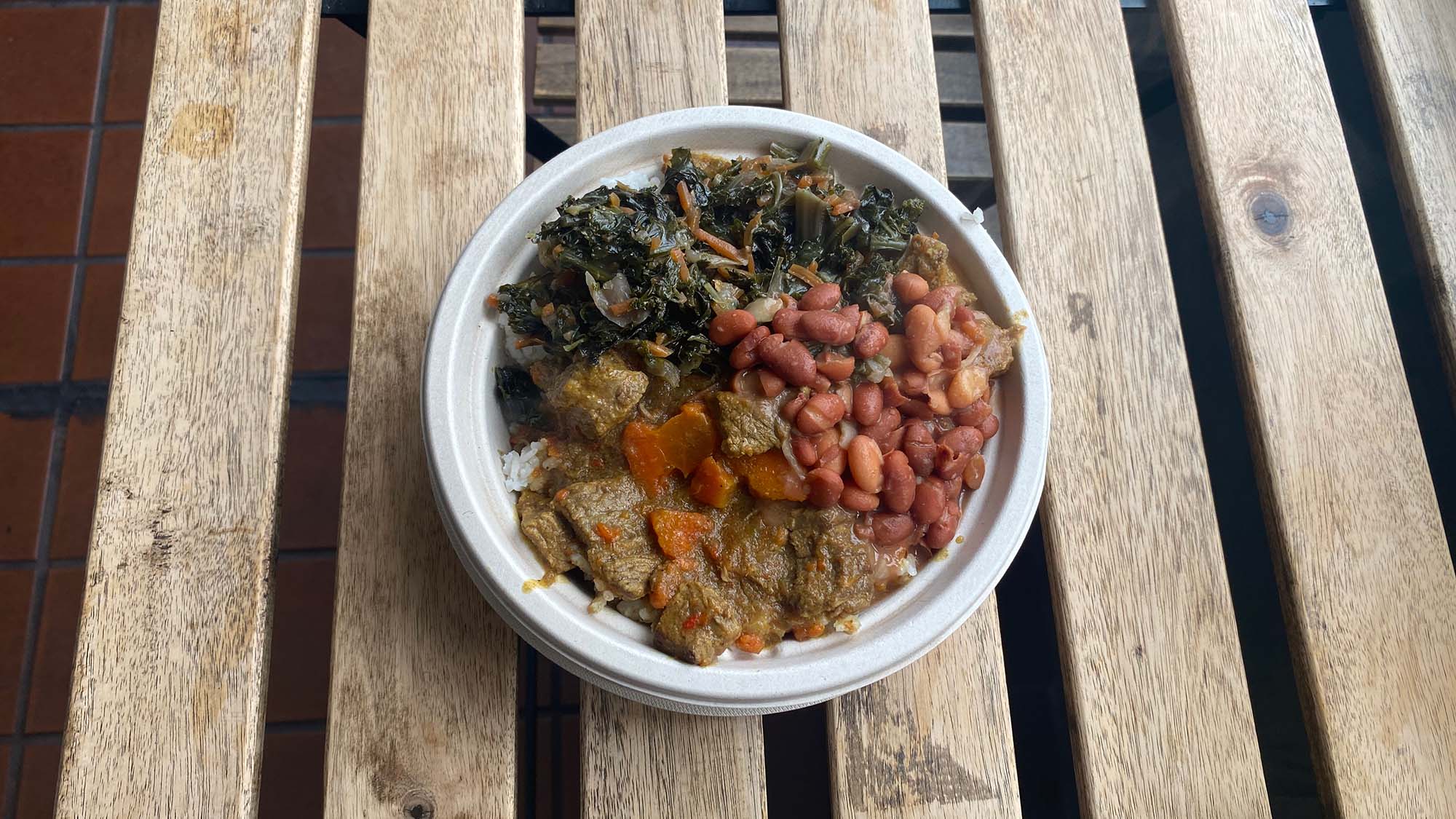 A curry rice bowl topped with beef, greens and beans.