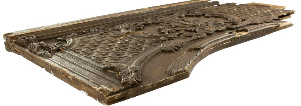 A piece of ornate wooden paneling, partially damaged and lying flat on the ground.