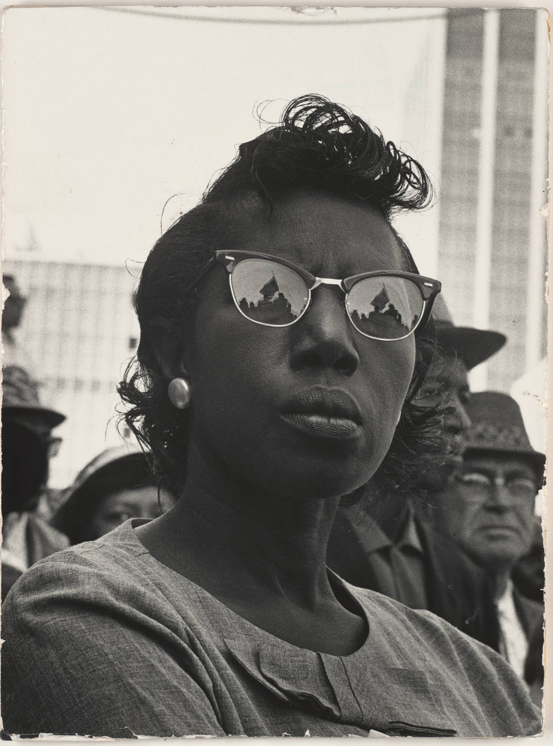 Black-and-white photo of American flag reflected in woman's glasses in a crowd