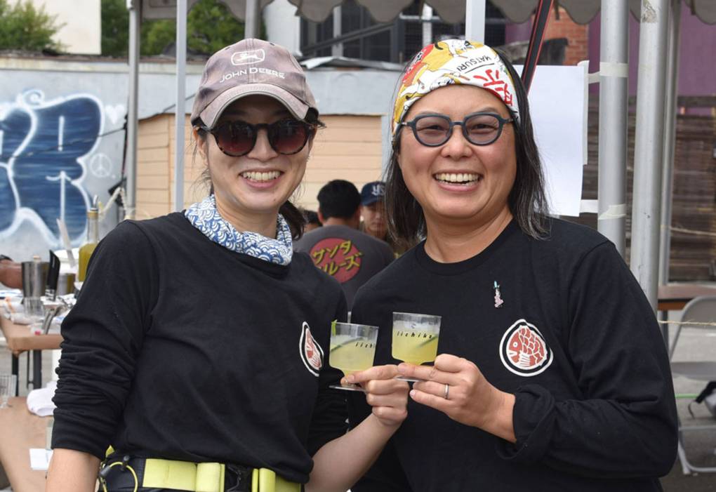two women stand outside and cheers with small glasses of sake