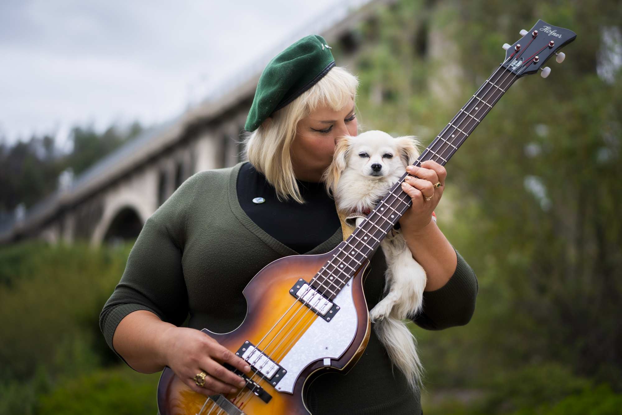 Woman kisses small dog while holding bass guitar