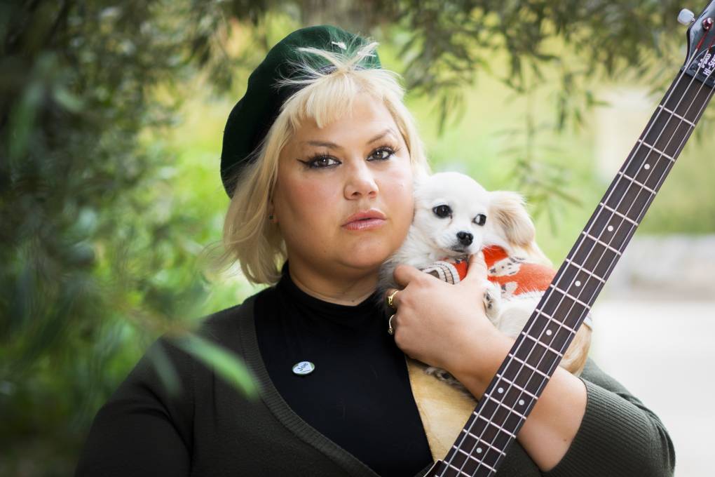 Blonde woman in black with bass guitar holds a small white dog