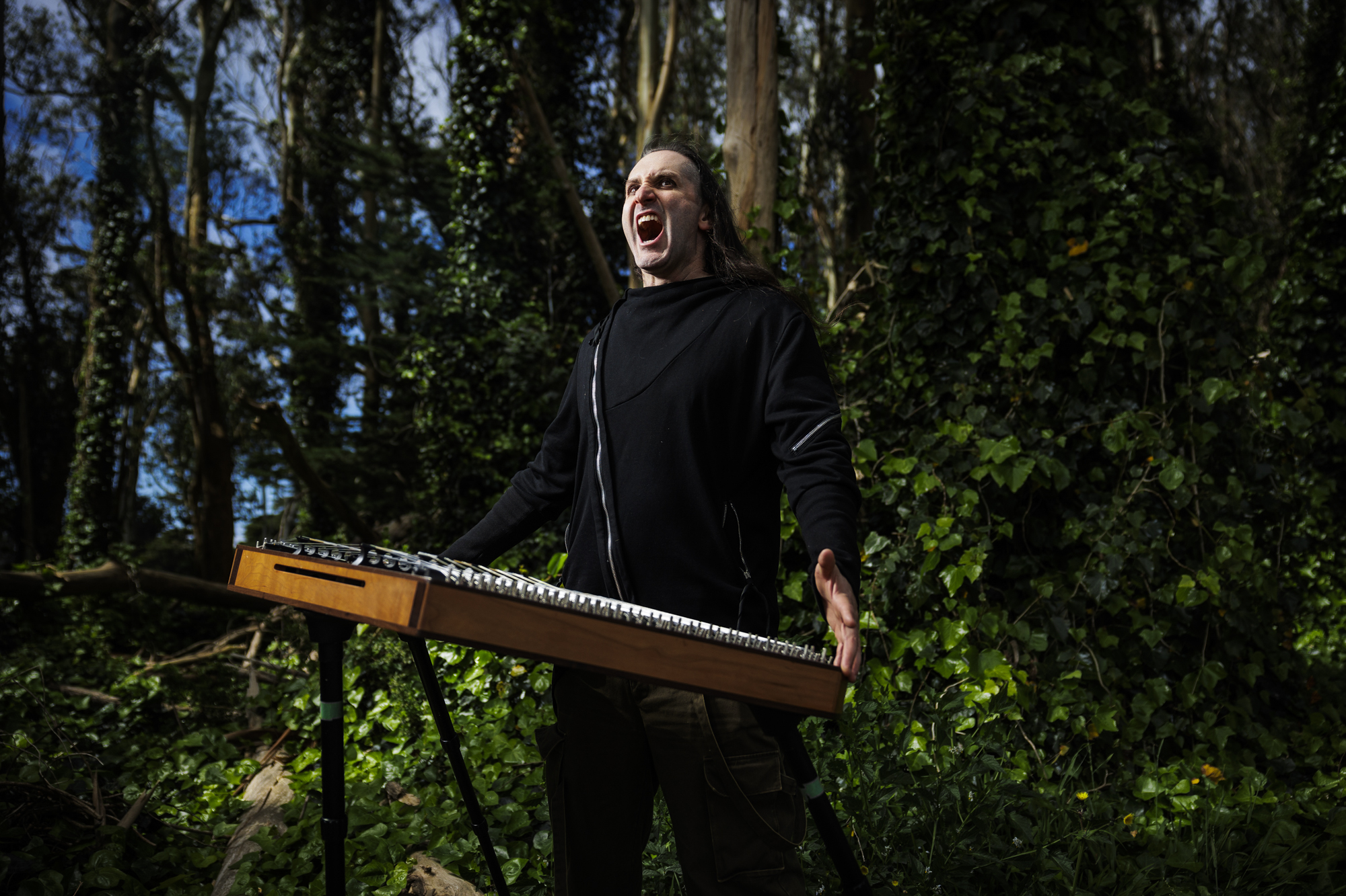 Botanist holds his hammer dulcimer while screaming in a eucalyptus grove.