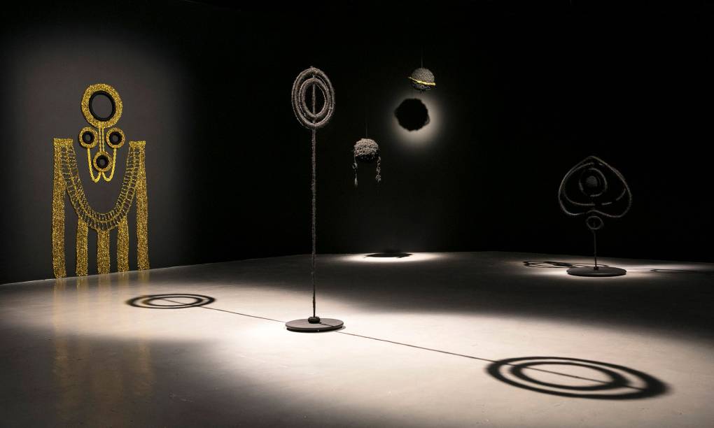 dark gallery space with spotlit sculptures of hair-covered loops and wall hanging