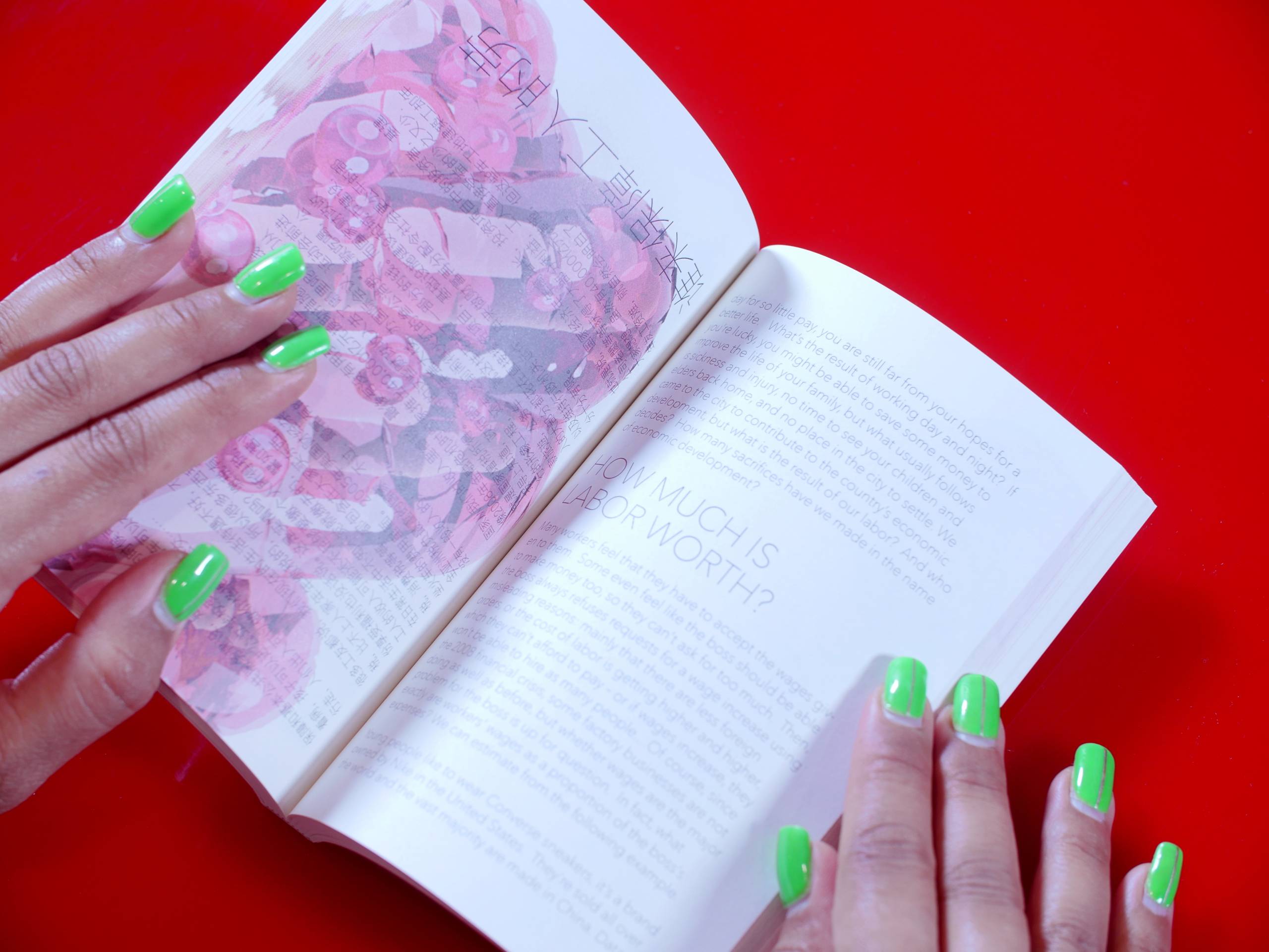 Two hands with green nails hold open a book against red surface