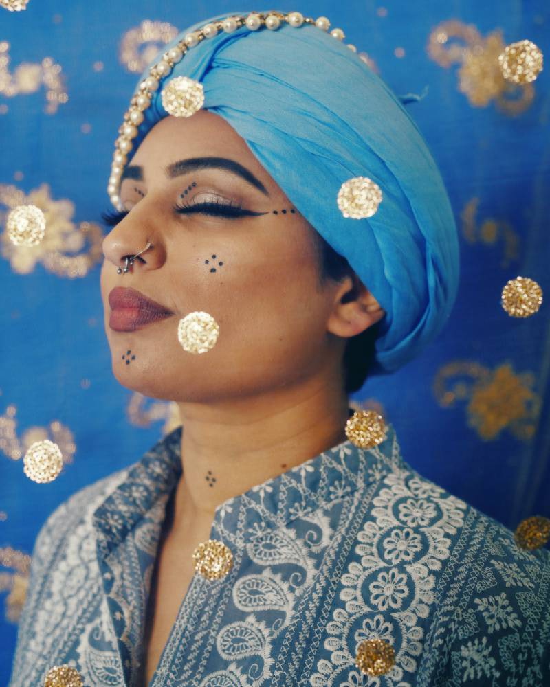 A profile shot of a non-binary person with their eyes closed wearing a light blue turban.