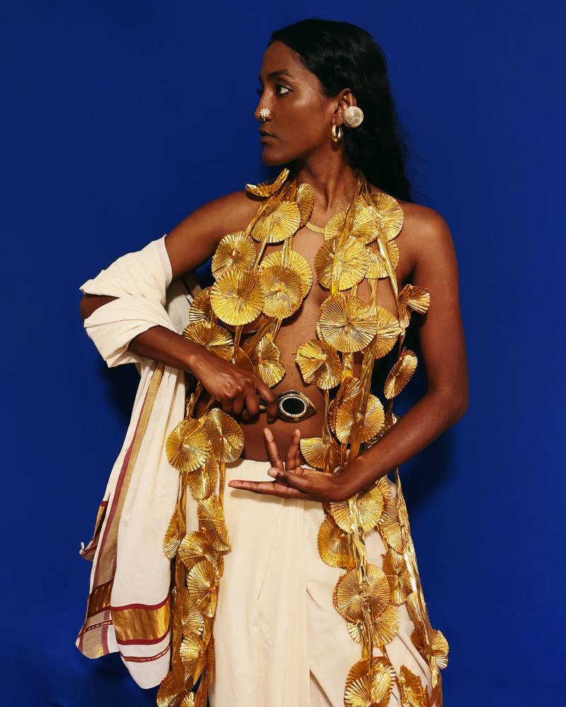 A profile shot of a person draped in a decorative gold top against a blue background.