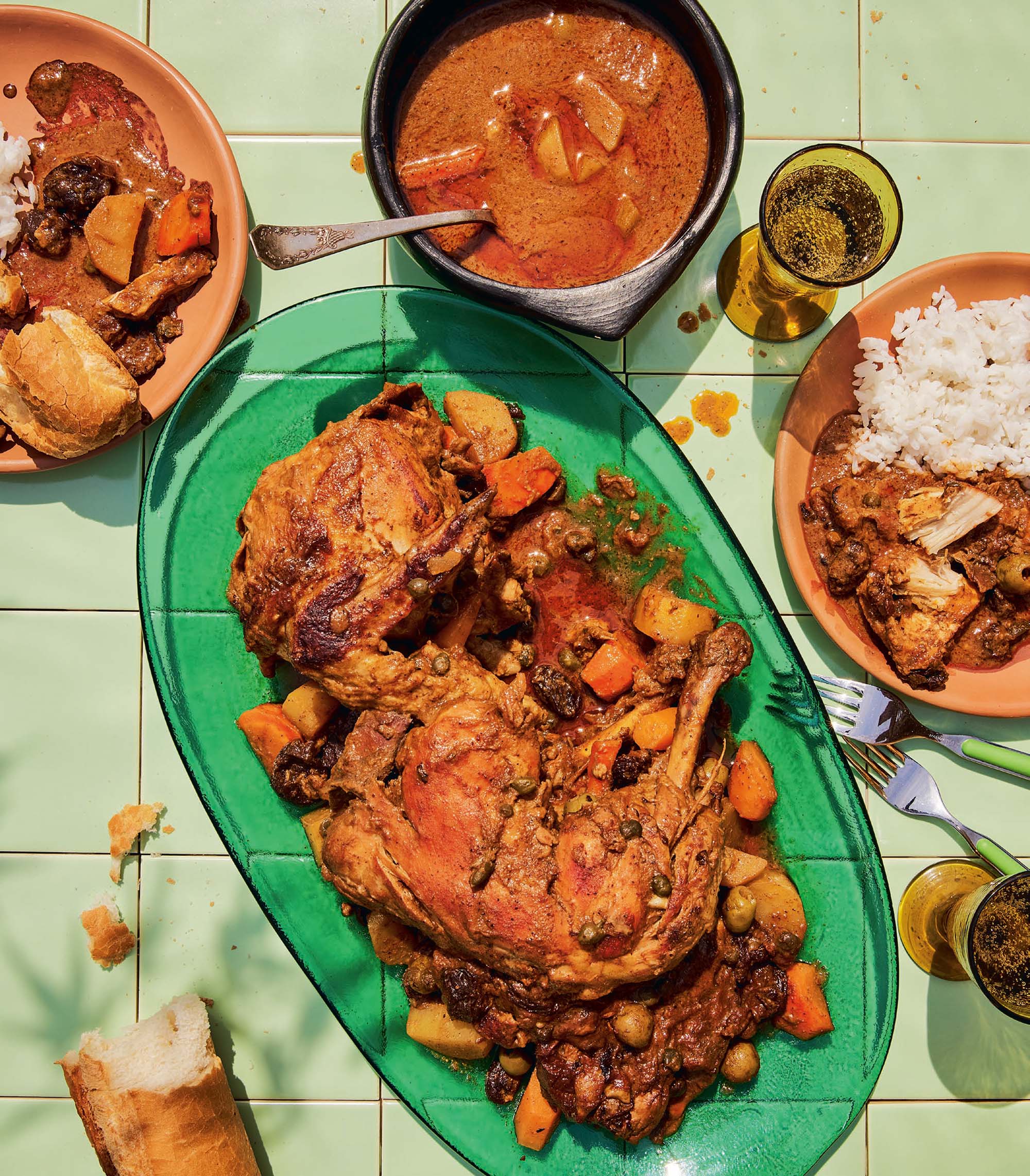 A stewed chicken served on a green platter surrounded by bowls of white rice.