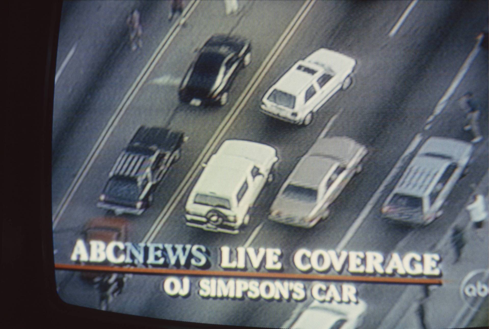 A photo of a tv screen showing cars lined up on a freeway. The caption says "ABC News Live Coverage. OJ Simpson's car."