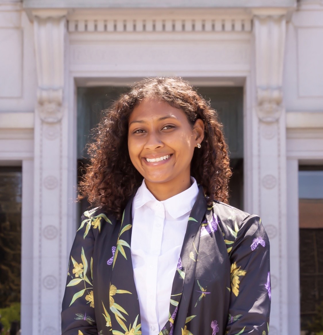 Nia Jones, the Energy Queen, poses for a photo while wearing a dark floral blazer and a white dress shirt.