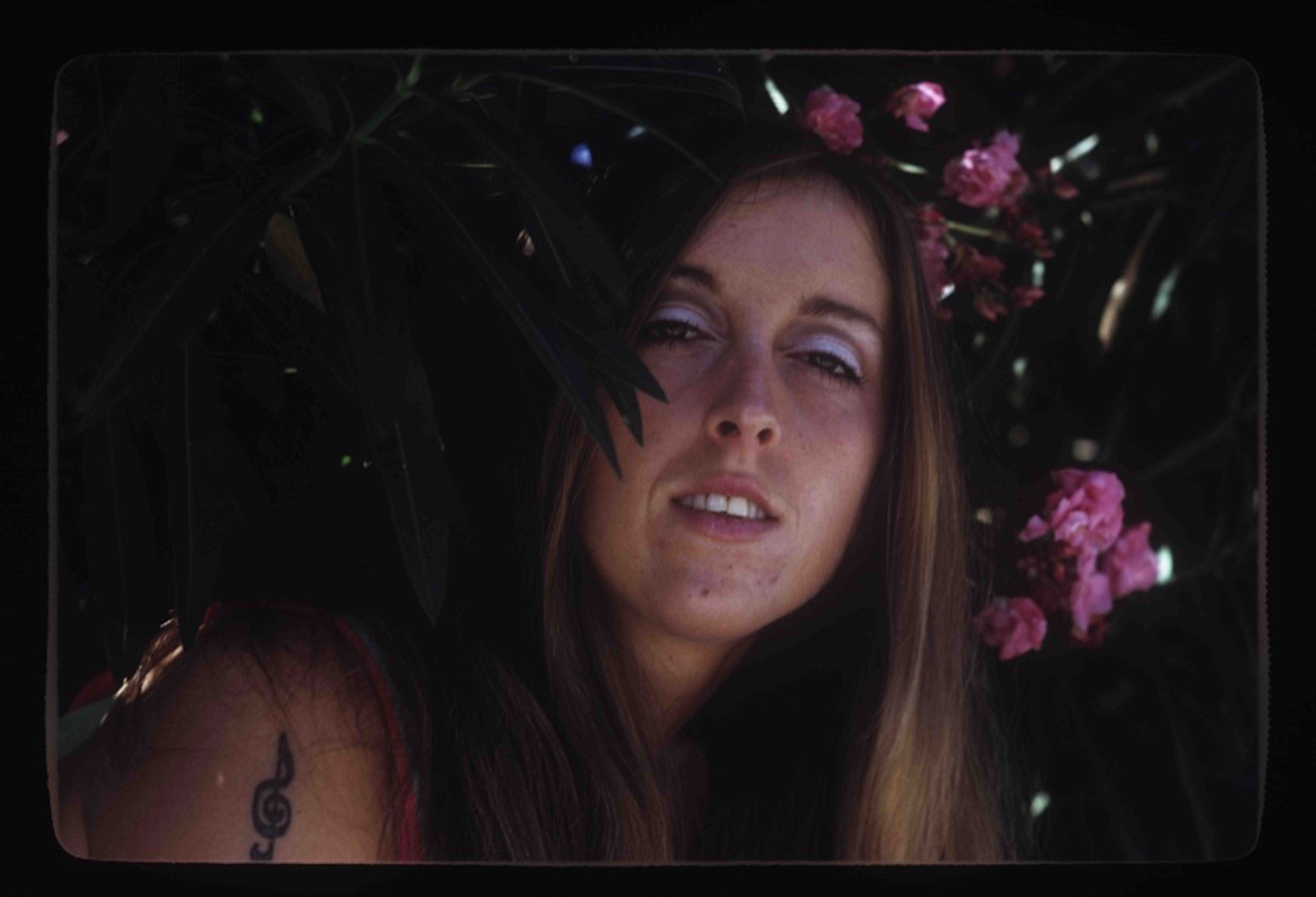 Person with long hair and blue eyeshadow set against flowering bush