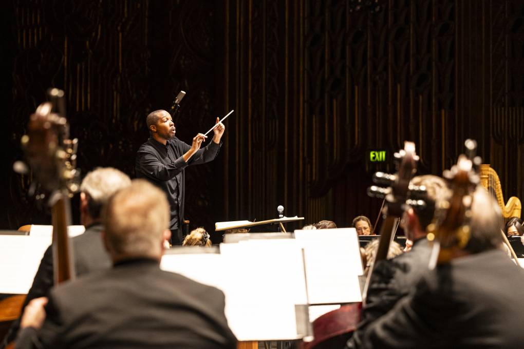 A conductor waves his baton as orchestra musicians look on,