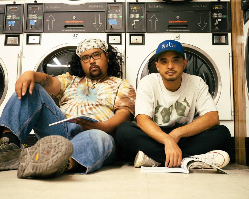 two young musicians sit in front of a washing machines at a laundromat