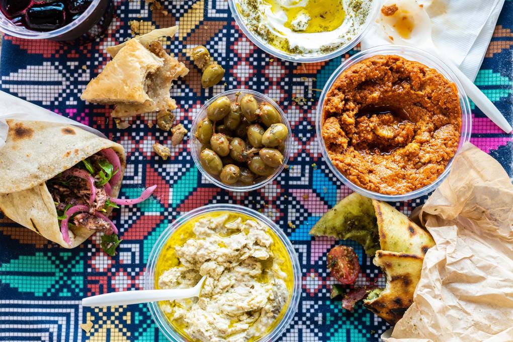 A spread of mezze, including olives and assorted dips and breads, all laid out on a colorful patterned tablecloth.