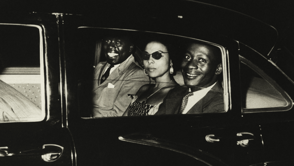 Black and white photograph of three people in backseat of a car, two smiling broadly