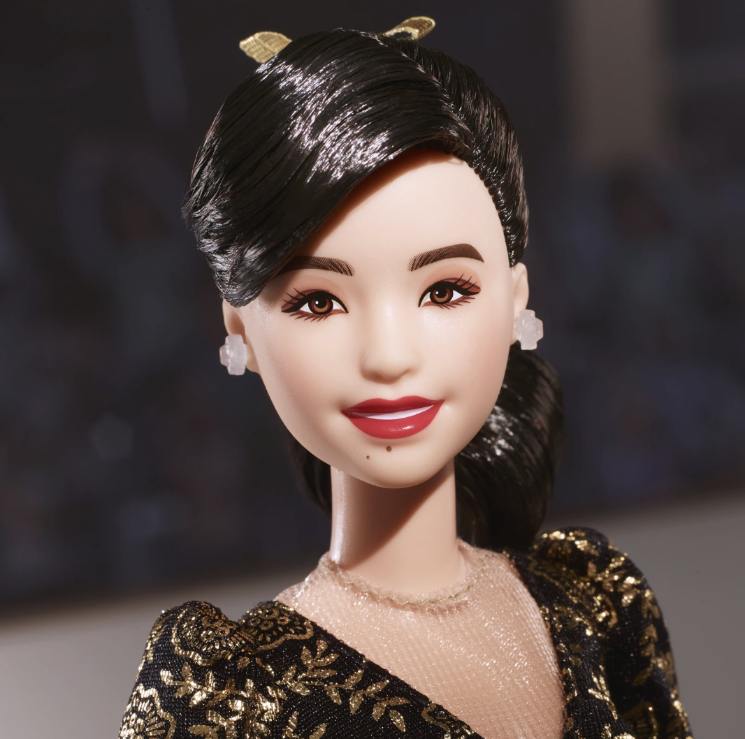Close up of a smiling doll's face with impeccably styled hair, wearing earrings.