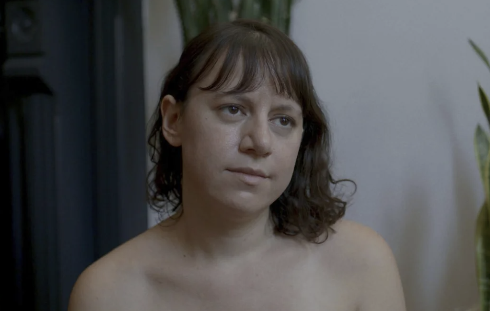 A topless white woman with brown hair, viewed from the shoulders up.