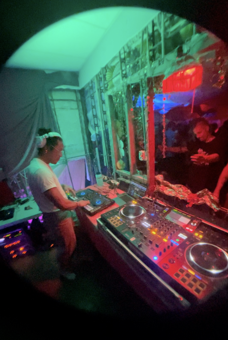 Adonis stands behind a set of turntables while DJing at an event in Oakland. 