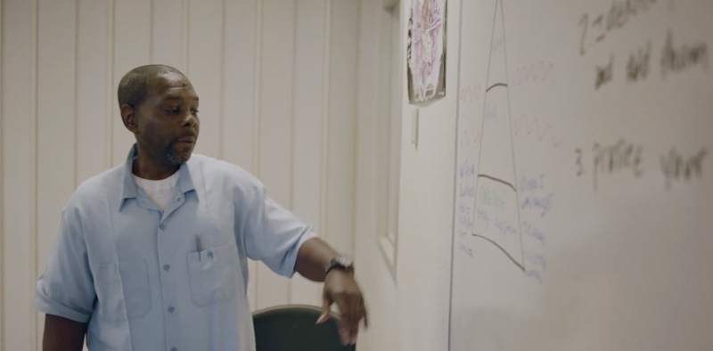 Anthony Hill, a mentor with California’s Offender Mentor Certificate Program, stands in front of a whiteboard discussing methods of personal healing. 