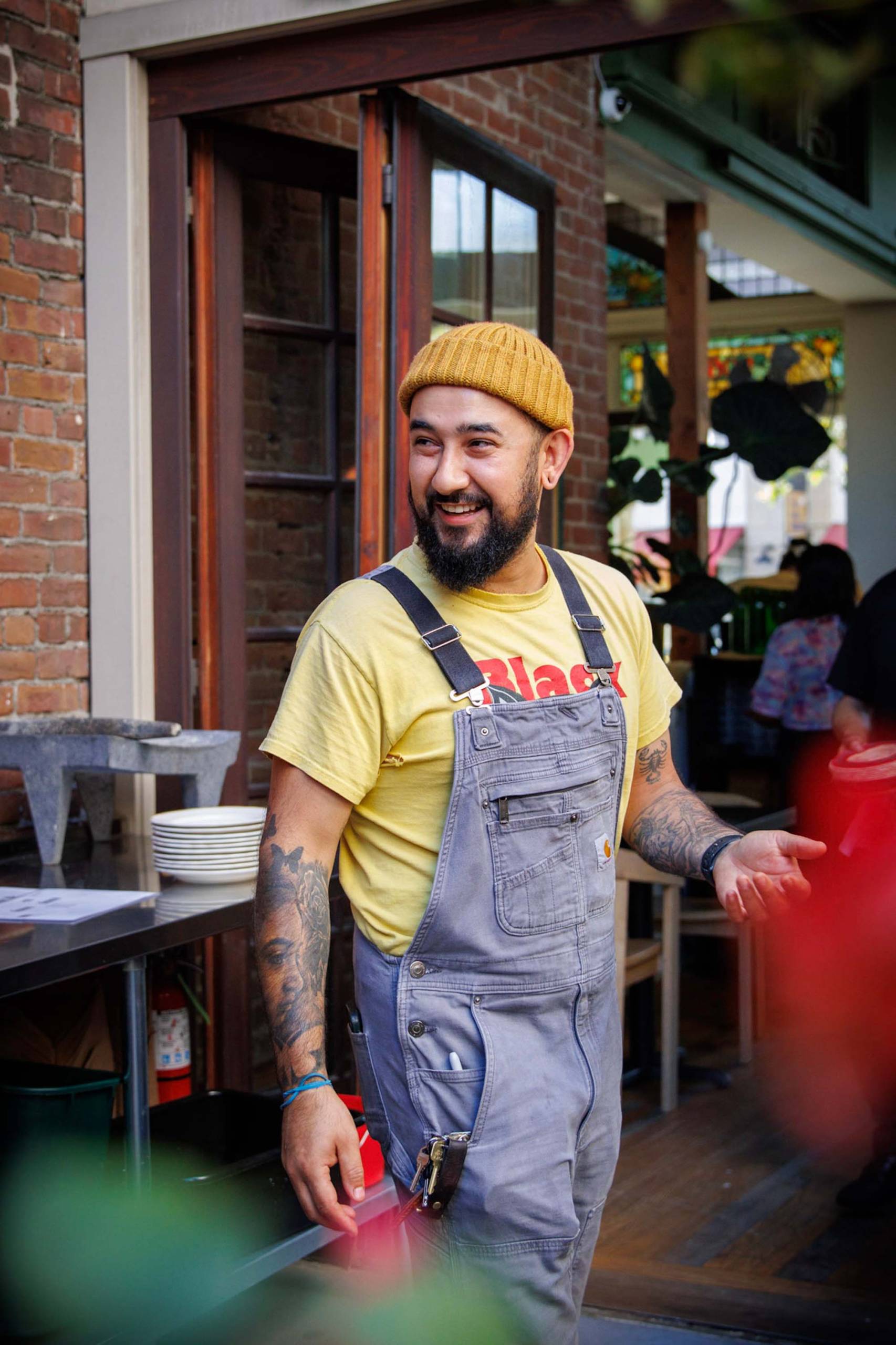 Portrait of a chef in overalls and a yellow beanie.