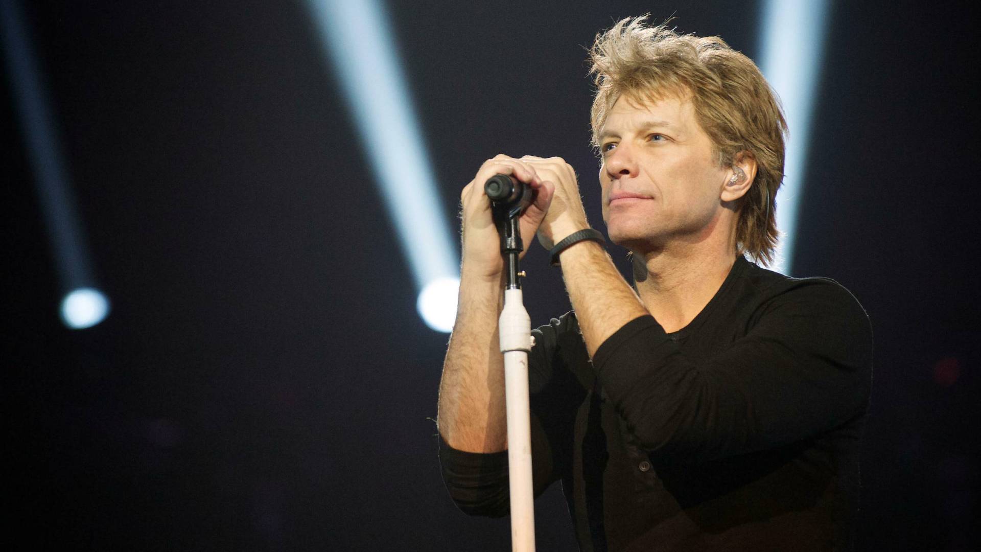 A middle-aged man stands behind a microphone looking pensive.