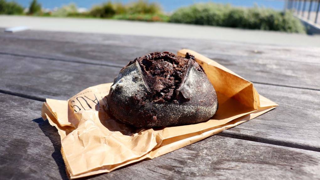 a loaf of chocolate sourdough is displayed on a wooden table outdoors