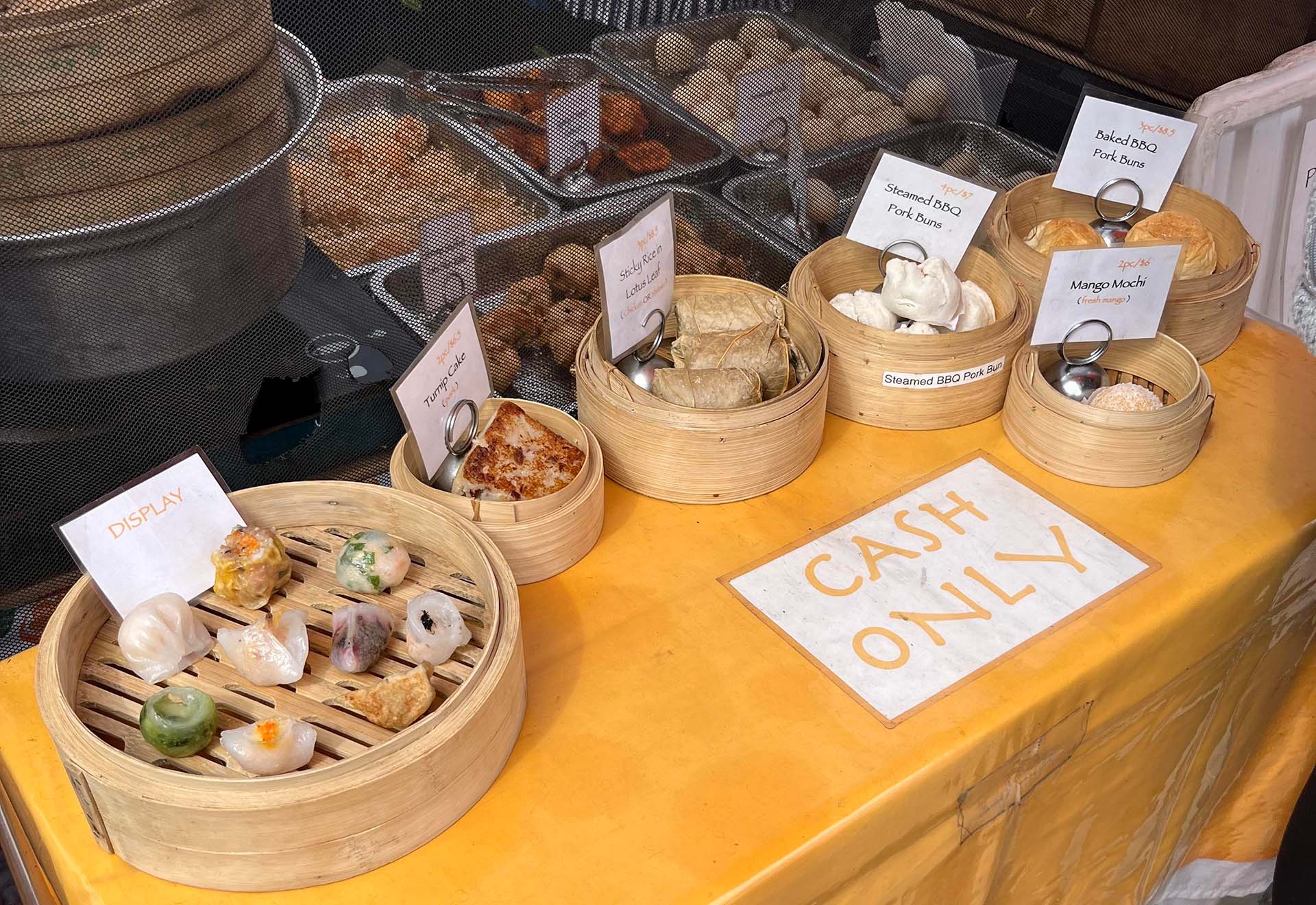 A display showing different kinds of dim sum available, all arranged in bamboo steamers. A sign on the table reads, "Cash Only."