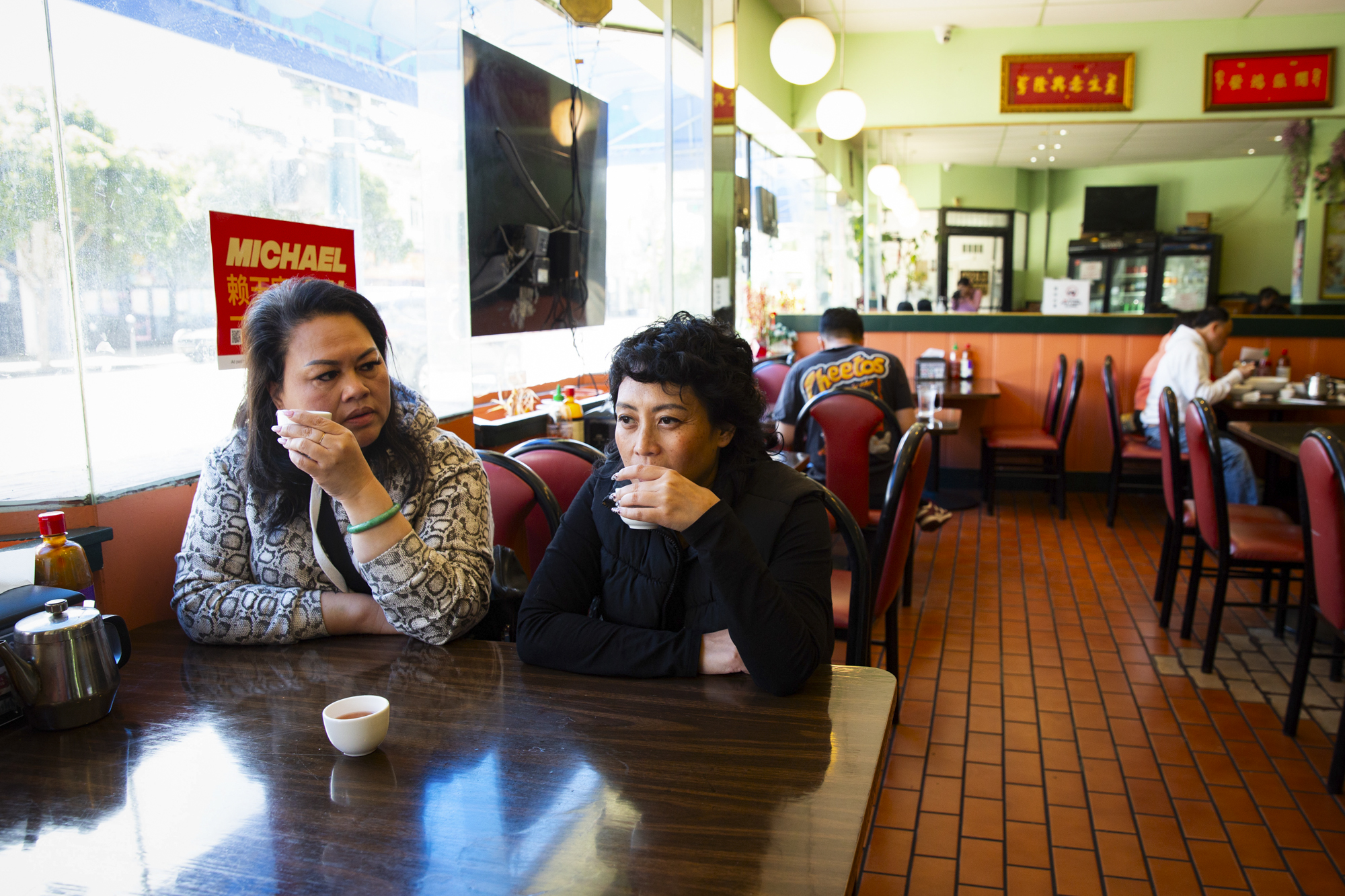 Two women sit at a booth and sip tea inside a restaurant.