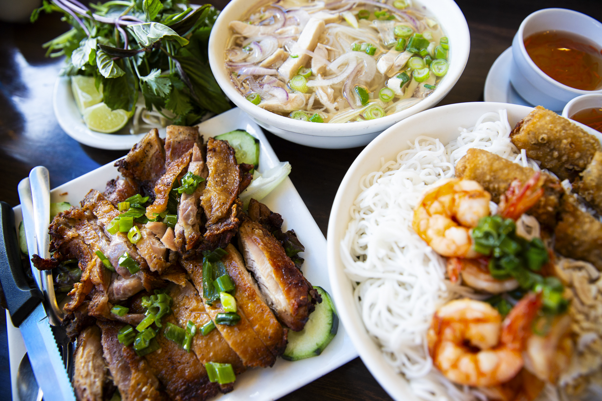 A spread of Vietnamese dishes, include pho, shrimp over vermicelli noodles, and grilled chicken thighs.