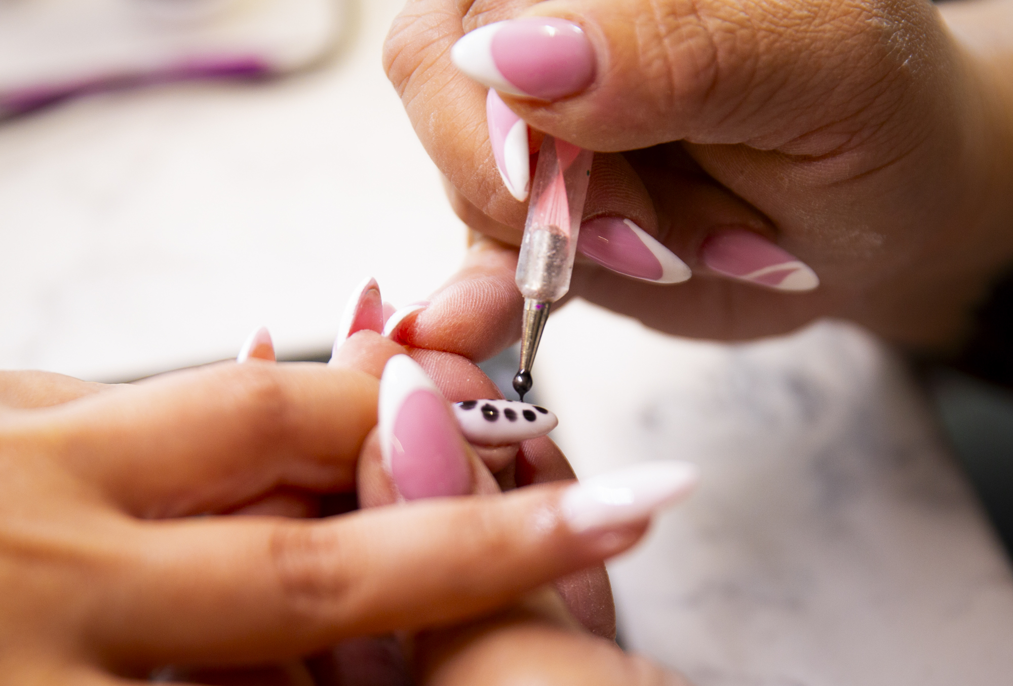 Close-up of nails being finished with a black dots on a pink design.