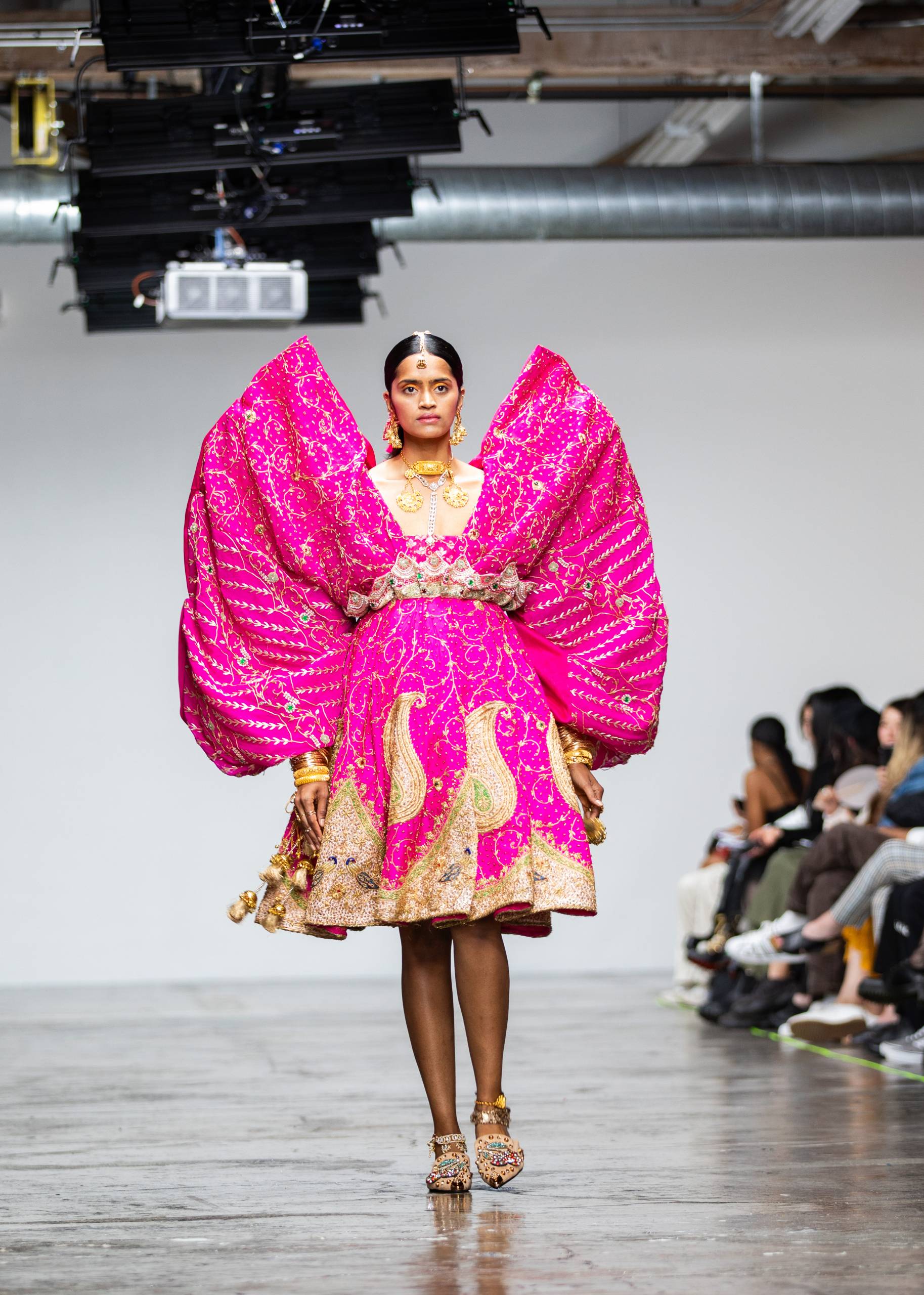 model in bright pink dress with giant sleeves and gold detailing