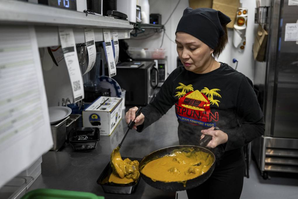 A woman in a black headwrap prepares Filipino food inside a restaurant kitchen.
