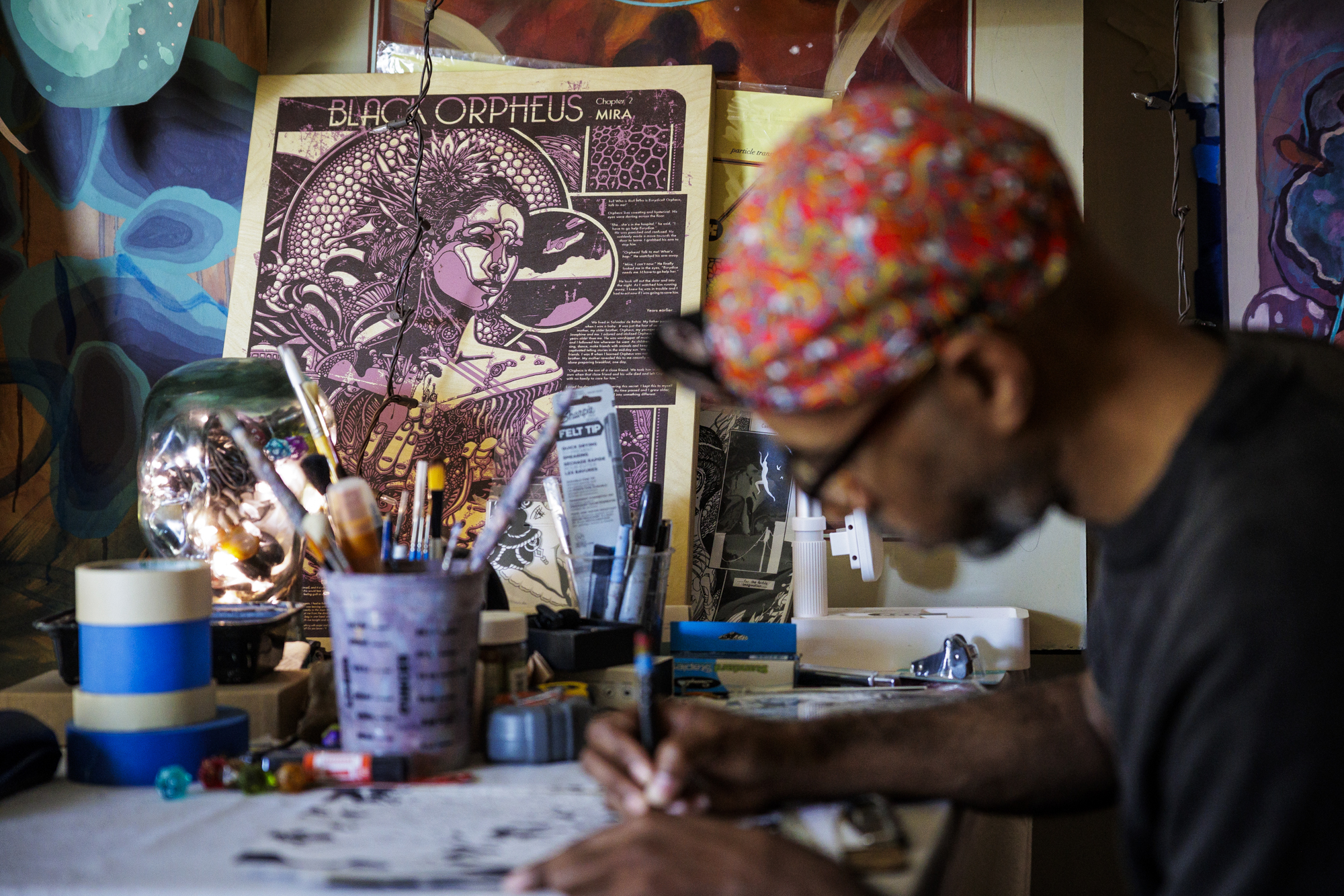 Black man leans over desk with pen in hand, materials behind