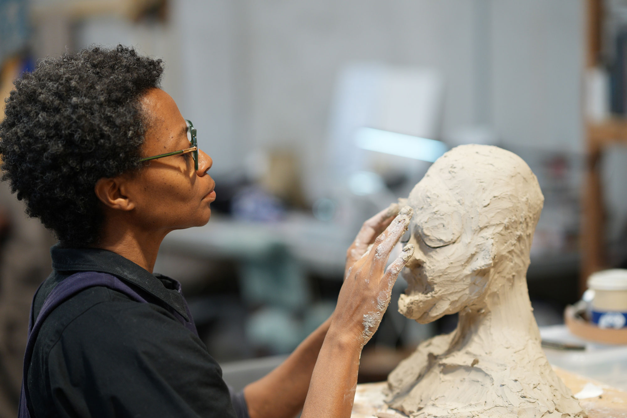 Black person works on a sculpture of a head with their hands