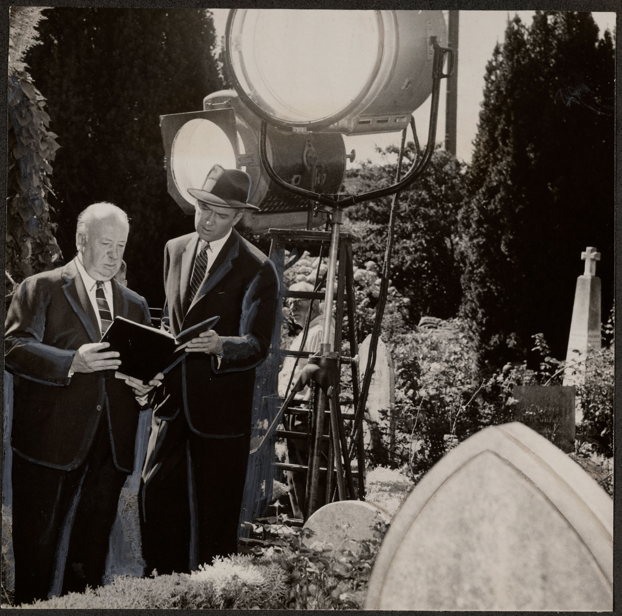 Black-and-white photo of two men looking at book with big spotlights behind them