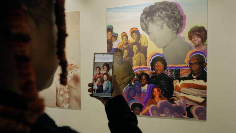 Person holds a cellphone camera up to a collage in a gallery displaying an augmented image
