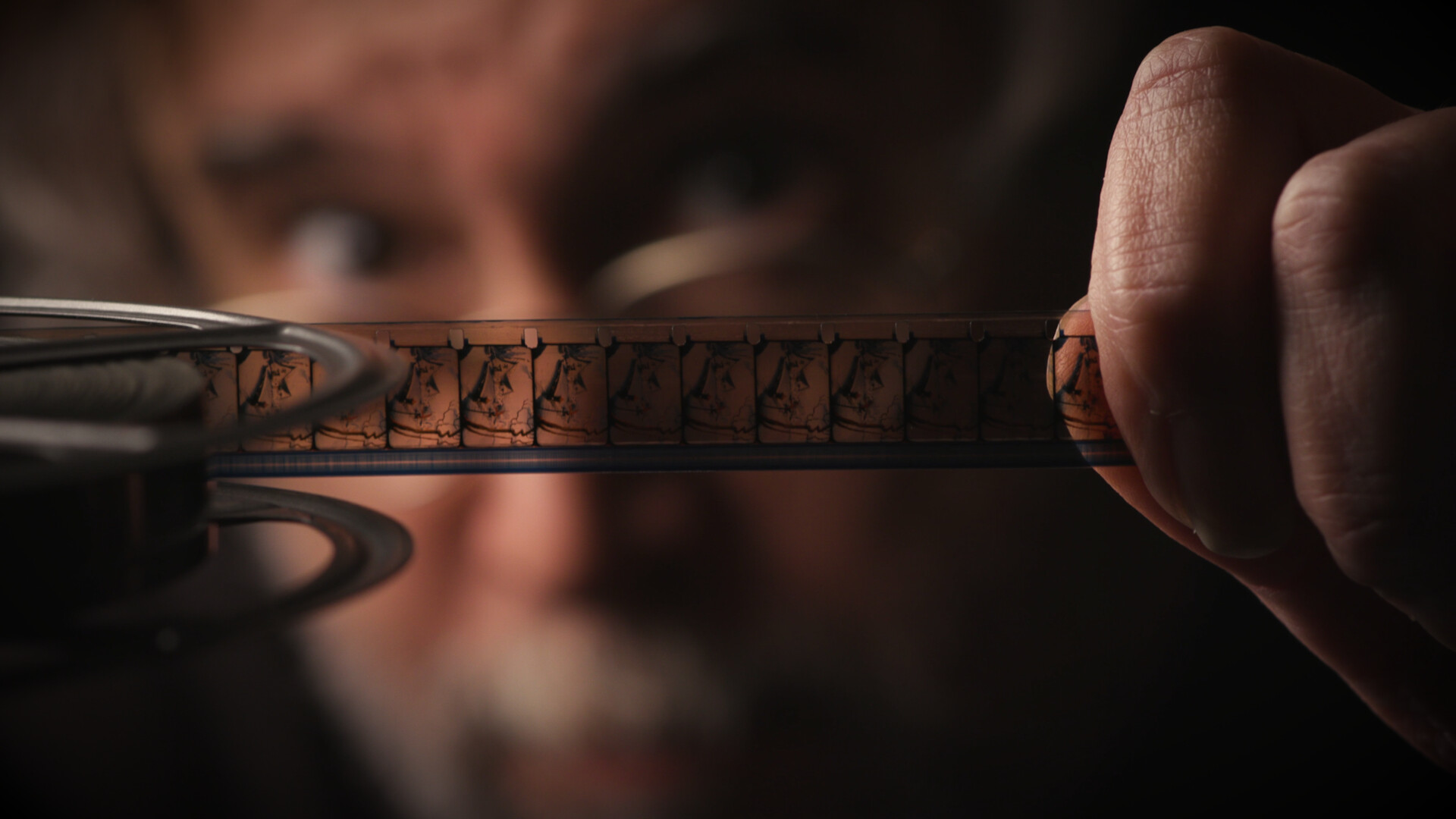 man holds strip of 16mm film in camera focus, his face out of focus