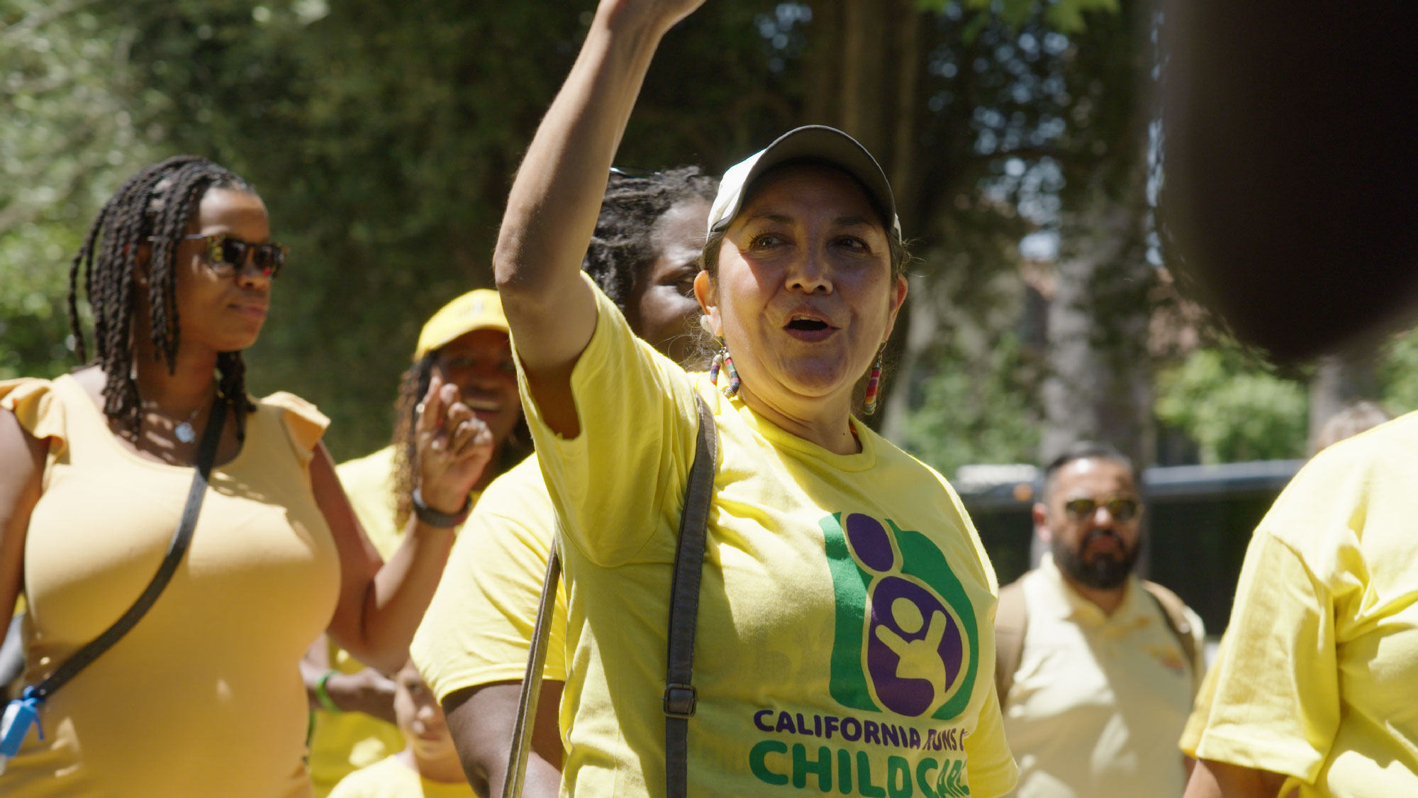 Woman in yellow logo shirt raises arm in a crowd other protesters