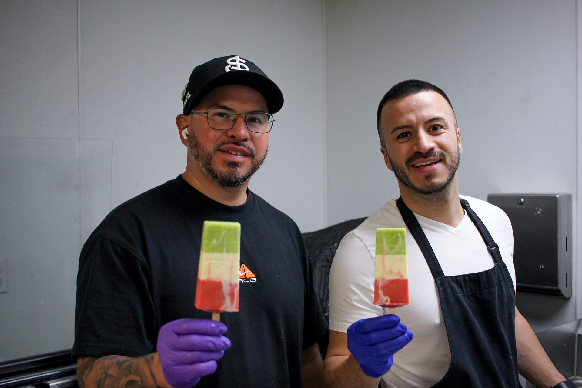 Two men in rubber gloves hold up popsicles.