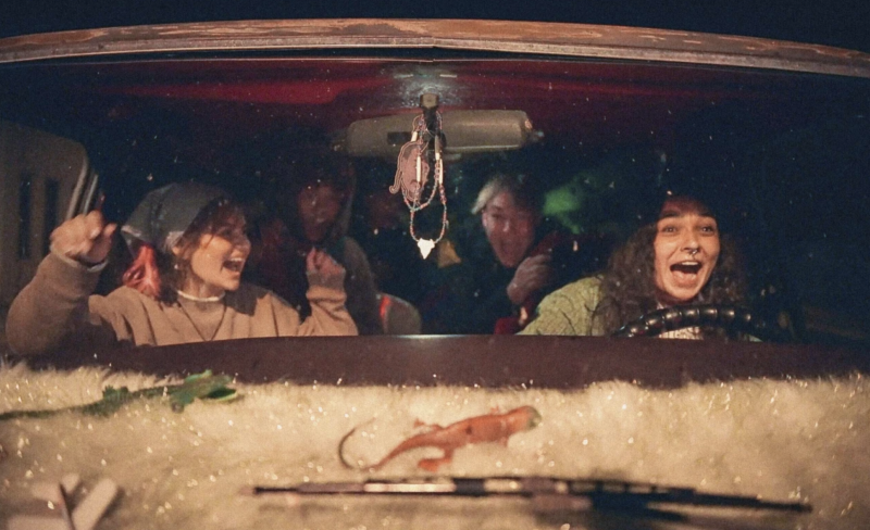 Two young women scream as they drive a car through the night.