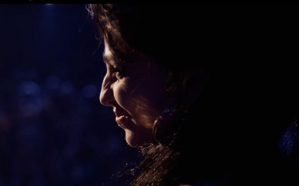 Side profile of a woman with stage lights on her face in a dark room.