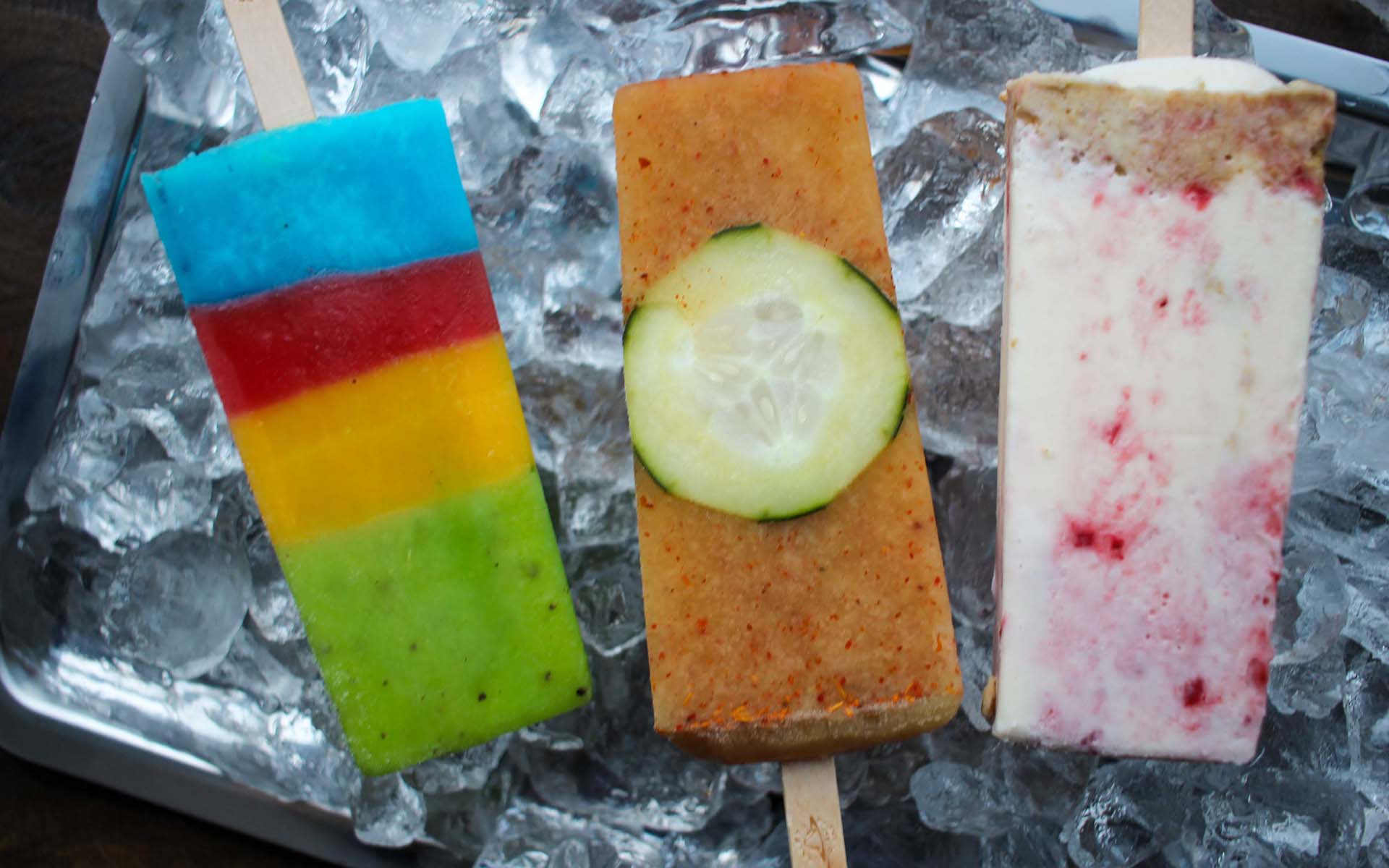 Three colorful Mexican popsicles on top of a tray of ice.