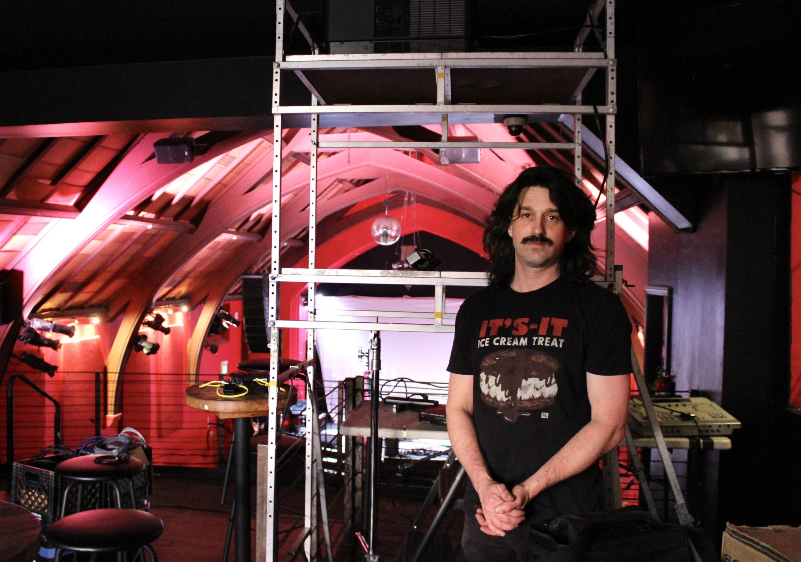 An artist poses in the south booth of a concert hall with a disco ball.