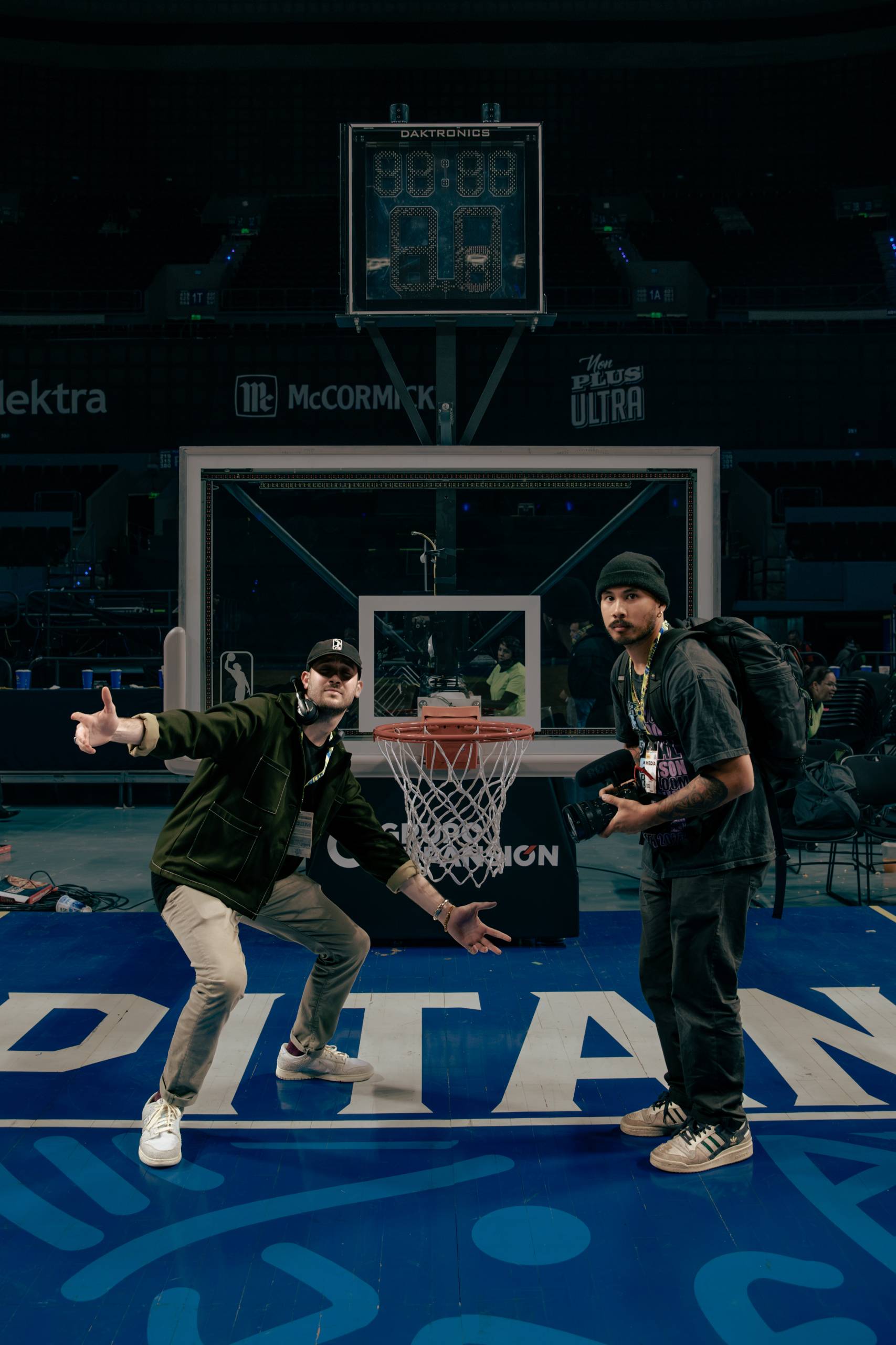 a film director and photographer pose on a basketball court in between filming