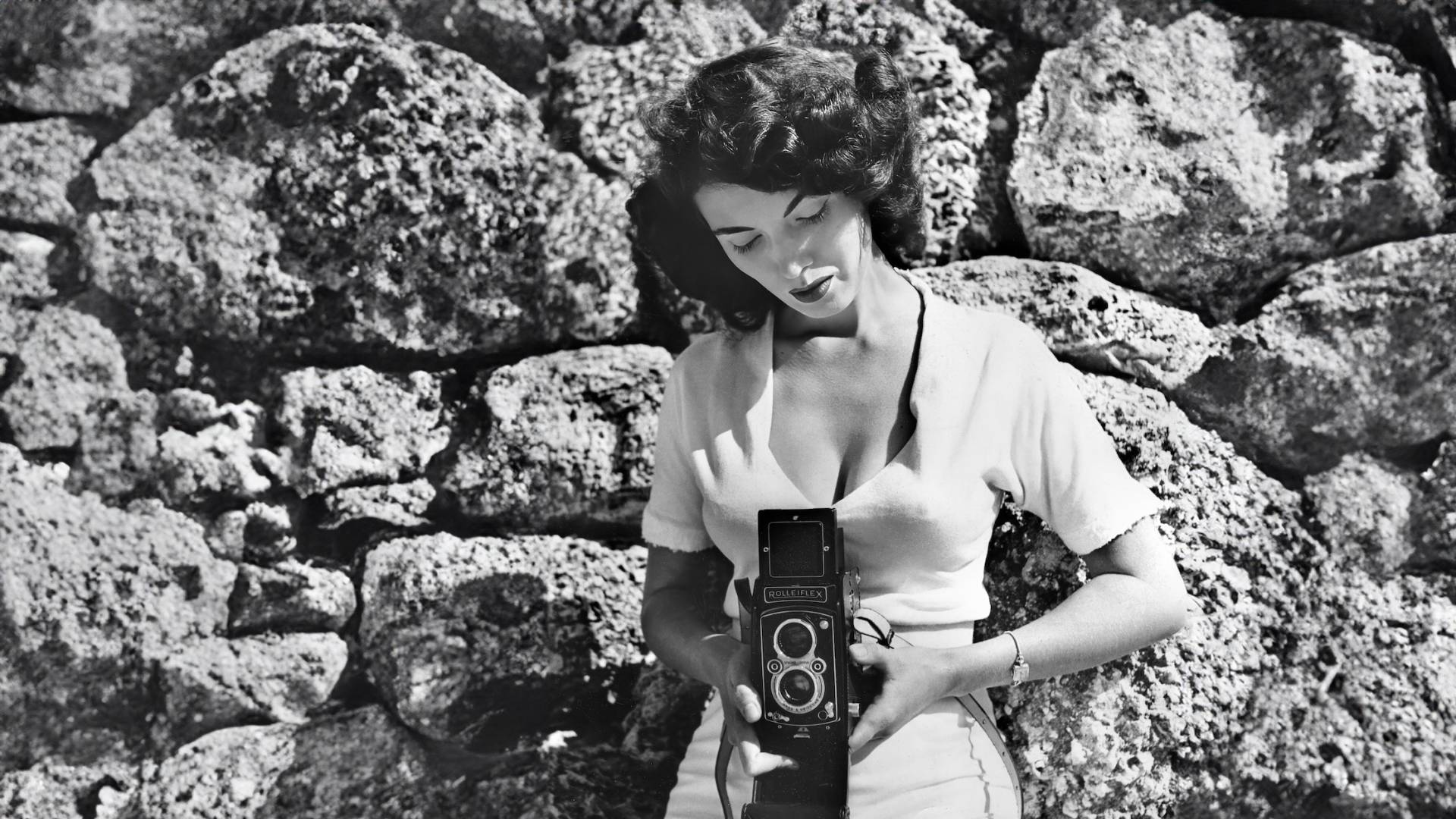 A beautiful 1950s-era woman wearing a low cut top, looks down towards her camera.
